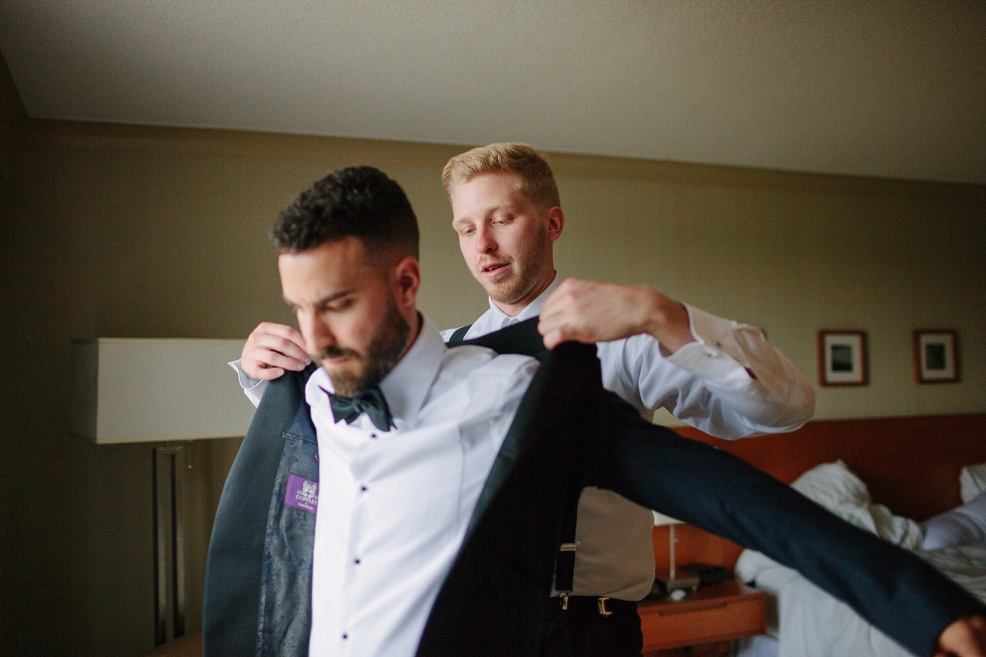 best man helping to put on groom's blazer