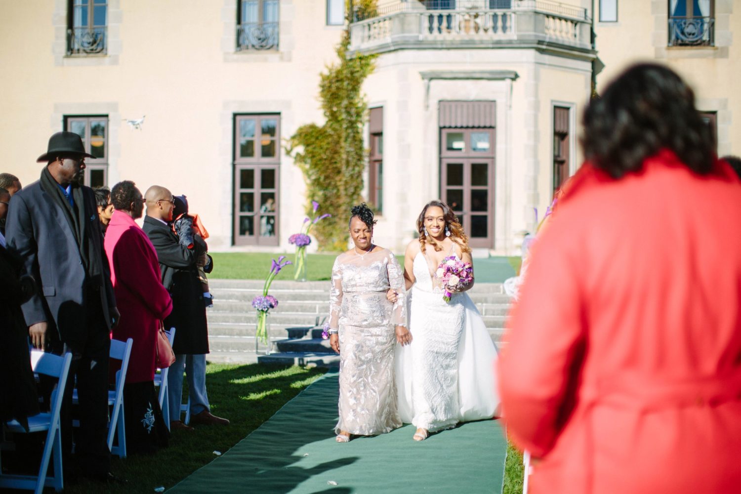 Bride and mother walking down isle outside of Oheka Castle.