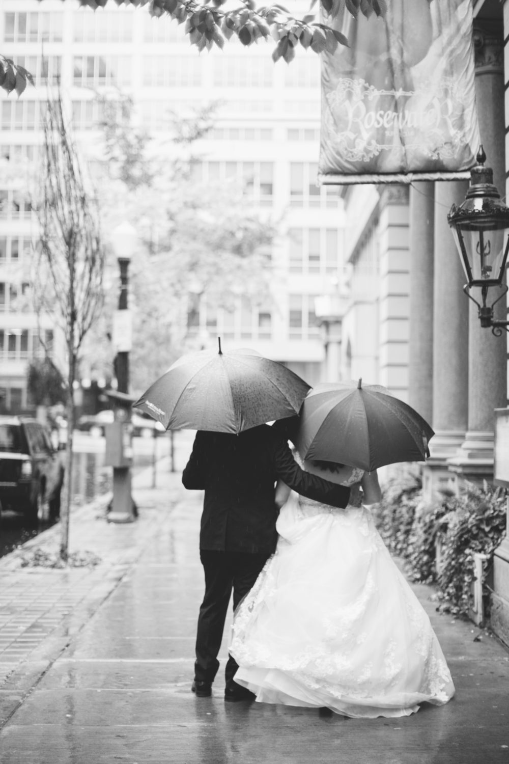 Wedding photography in the rain, couple walking down a street holding umbrellas.