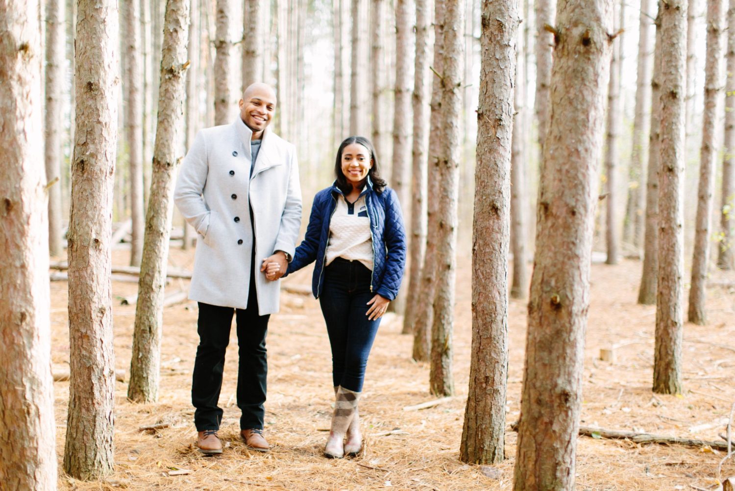 A couple holding hands facing the camera surrounded by tall birch trees at Kortright Centre.