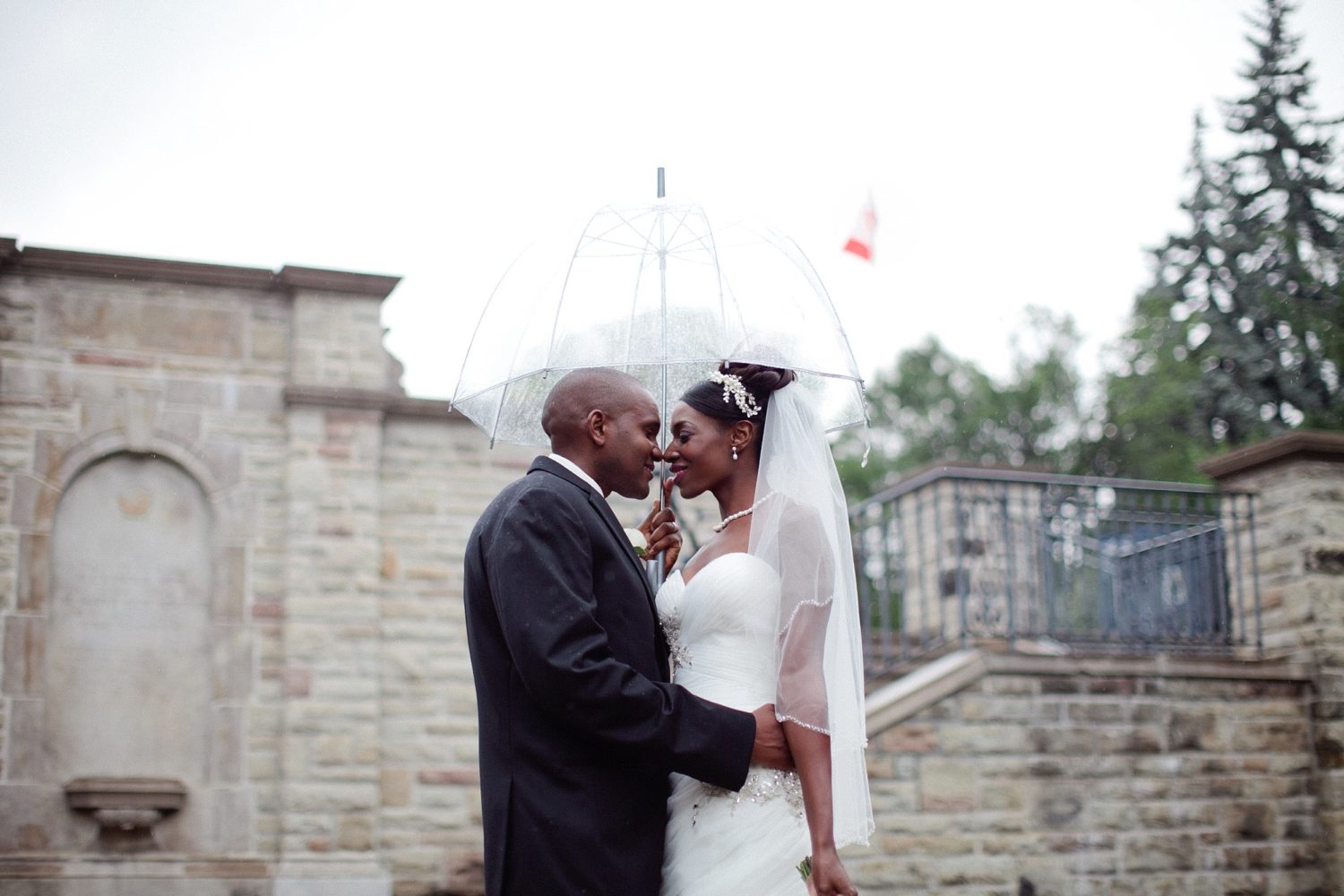 Wedding photography in the rain, couple standing under clear umbrella.
